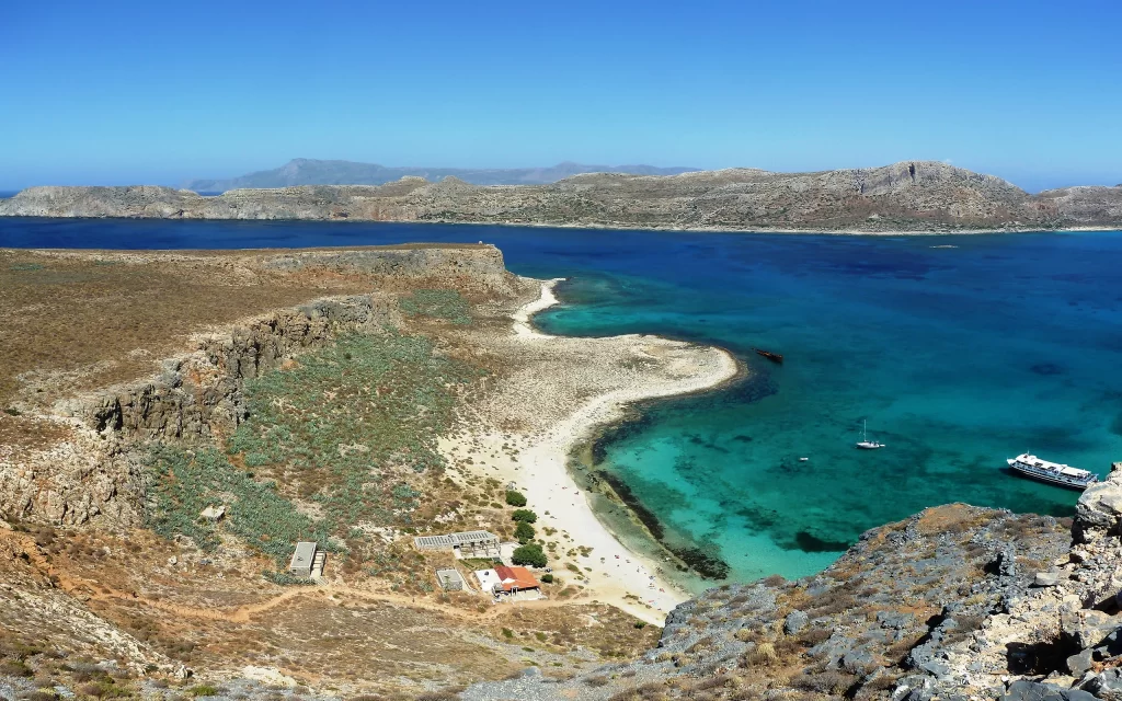Coastal landscape turquoise sea rugged cliffs sandy beach clear sky distant mountains