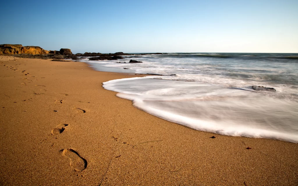 Footprints Sandy Beach Ocean Waves Rocky Shoreline Blue Sky