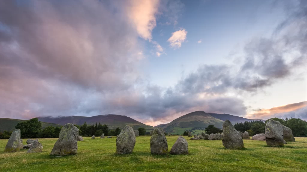 Stone circle green grass mountains sunset clouds ancient