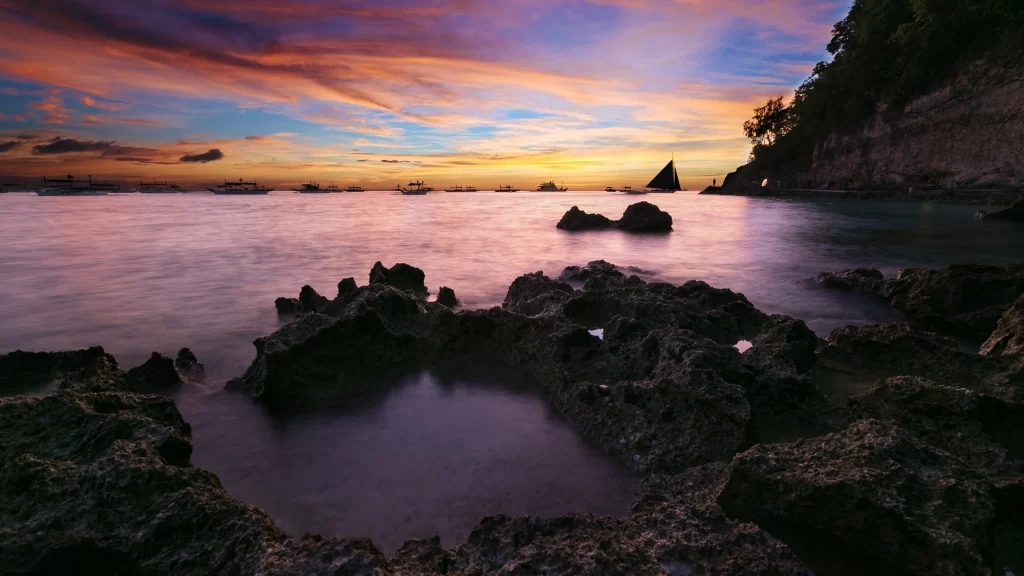 Sunset ocean rocks sky clouds sailboat