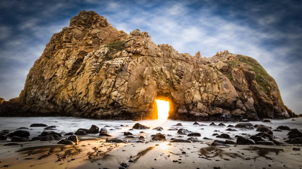 Sunset rock formation beach ocean natural arch golden light dramatic sky coastal