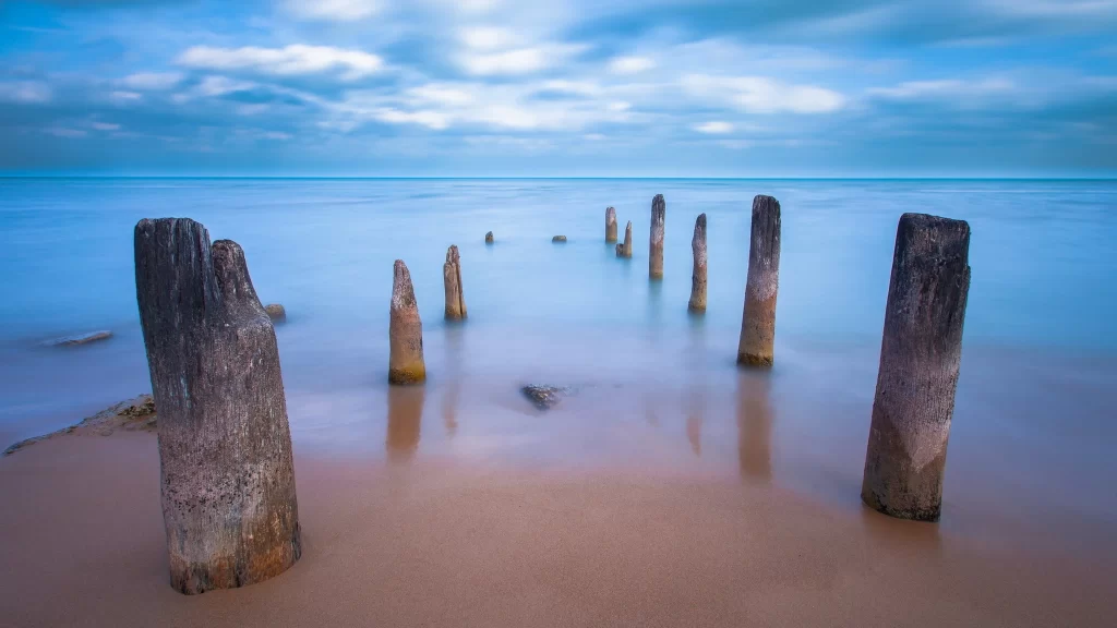 beach ocean sky clouds wooden posts water horizon tranquility