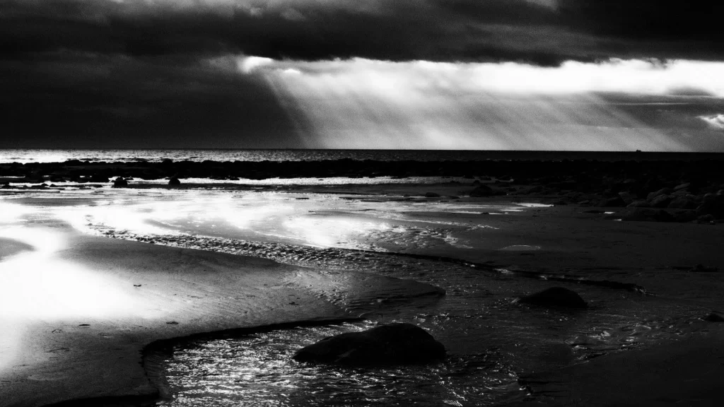 beach sunlight clouds water rocks black and white