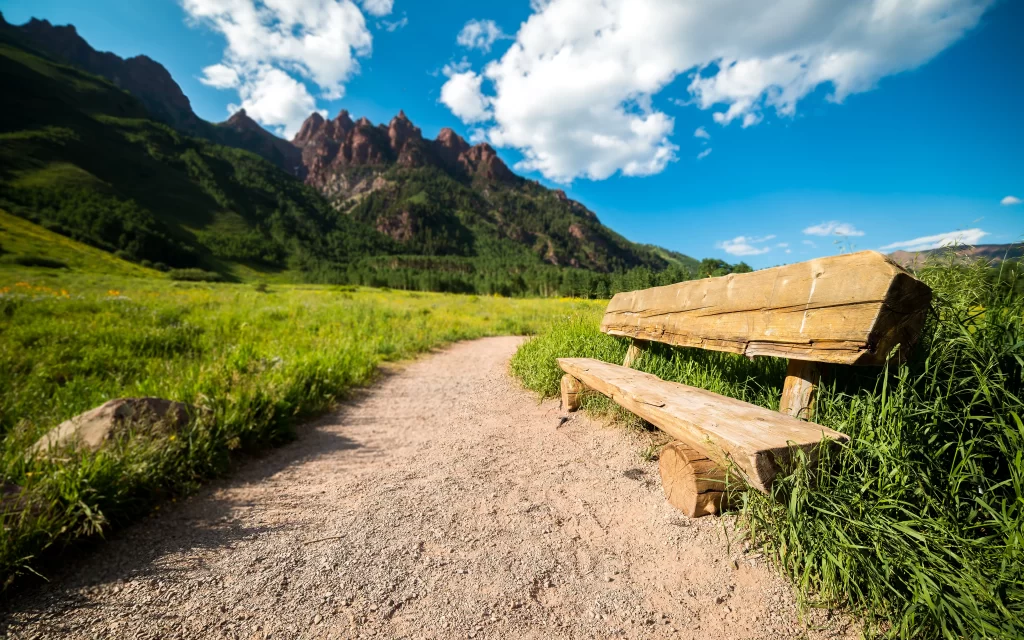 bench path grass mountains sky clouds