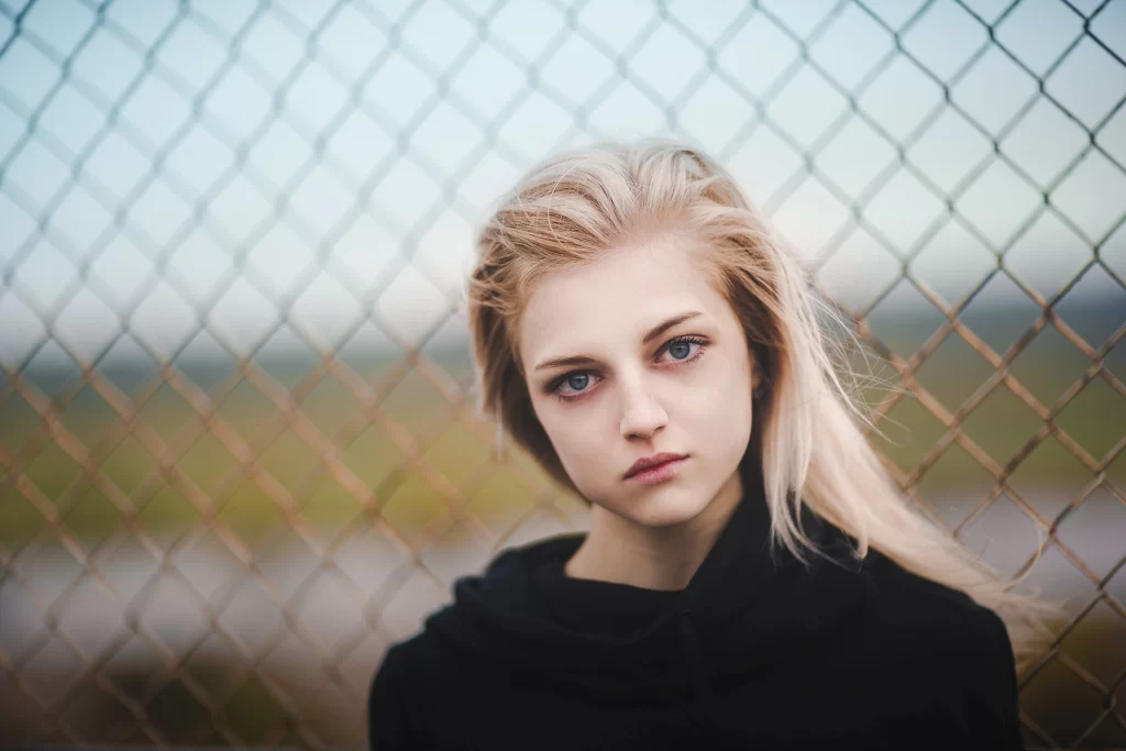 blonde hair black top chainlink fence outdoor setting blurred background natural