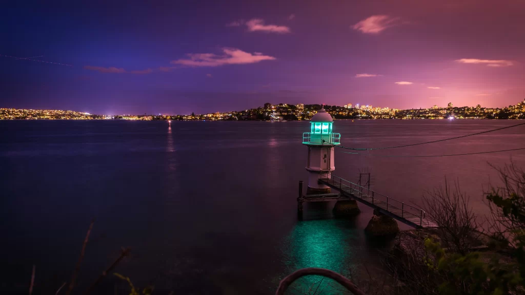 lighthouse night water city lights sky clouds