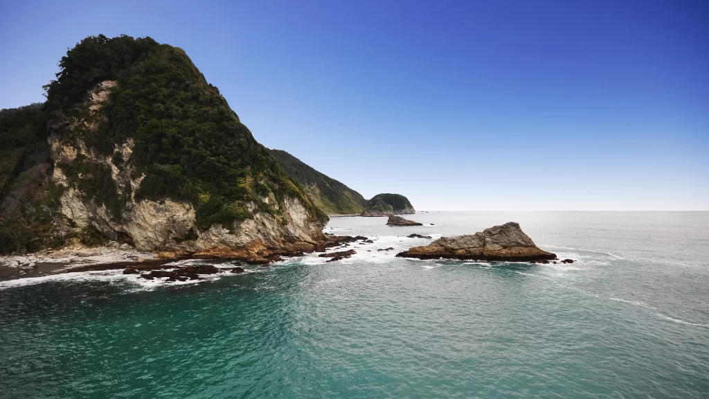 ocean rock cliff greenery waves sky