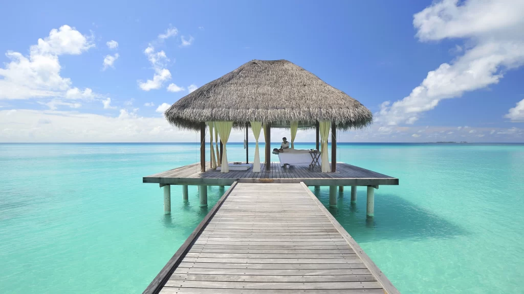 overwater bungalow wooden deck turquoise water blue sky thatched roof serene