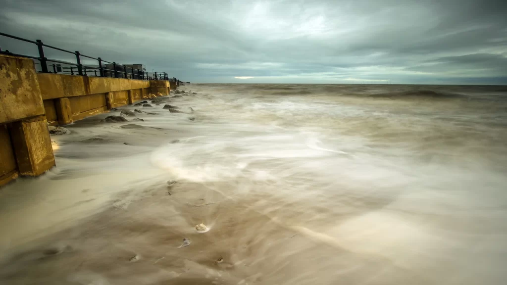 stormy sea cloudy sky waves concrete pier railing rocky shore