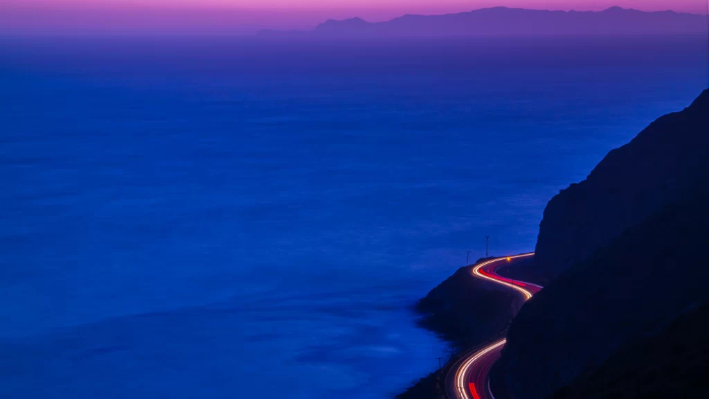 twilight coastal road ocean mountain light trails