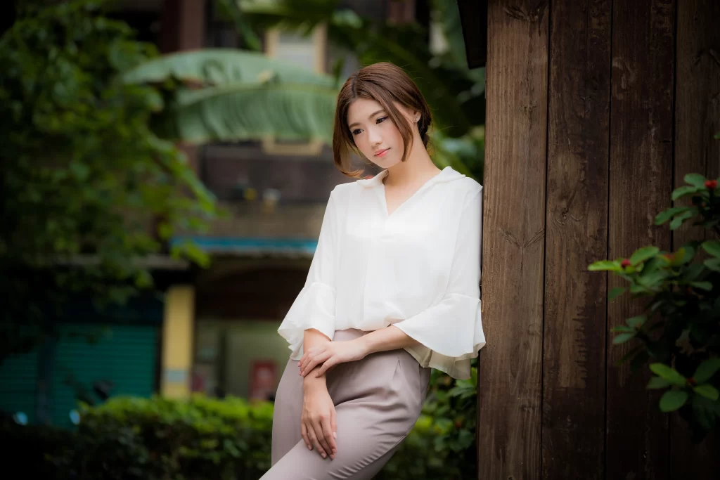 woman white blouse brown pants wooden wall green plants outdoor casual relaxed