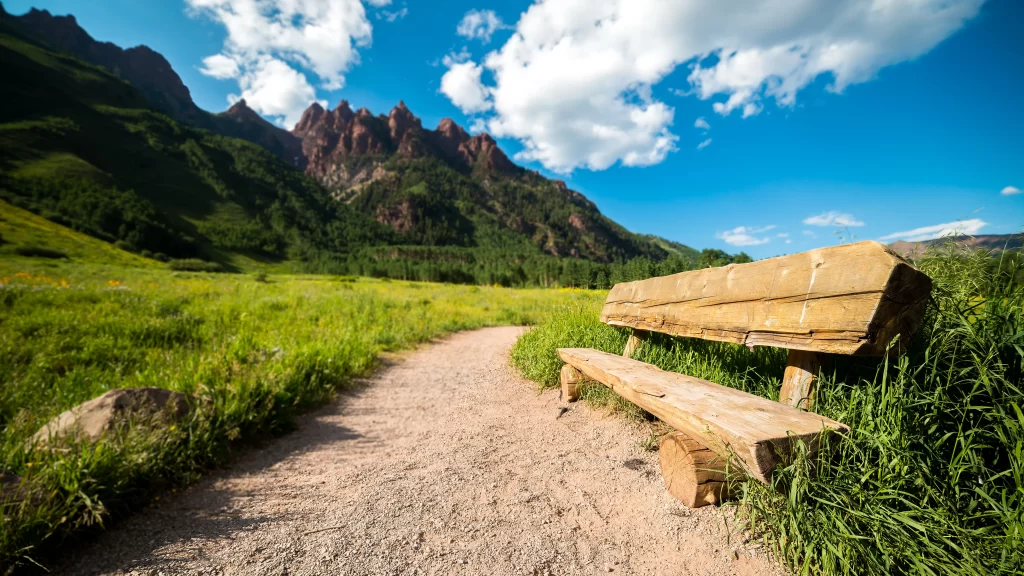 Wooden Bench Dirt Path Green Grass Mountains Blue Sky Clouds