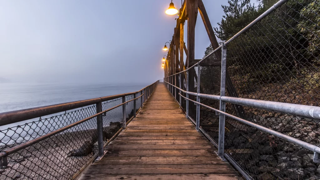 wooden bridge metal railing street lamp foggy calm water rocky shore