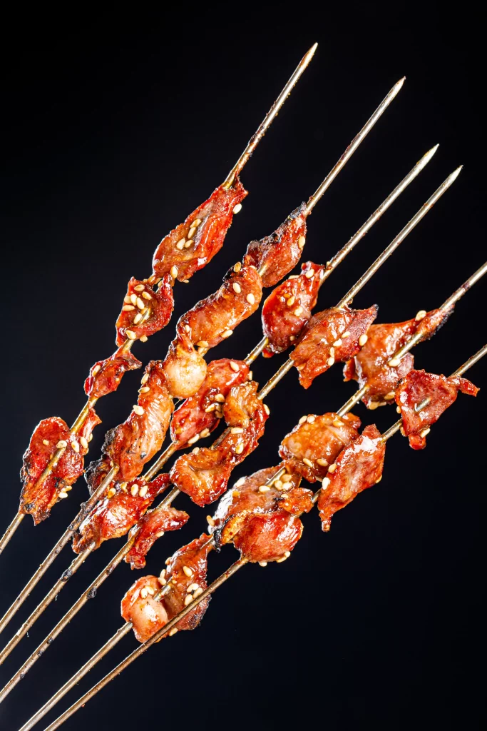Crispy Pork Skewers Charred Edges Golden Brown Sesame Garnish