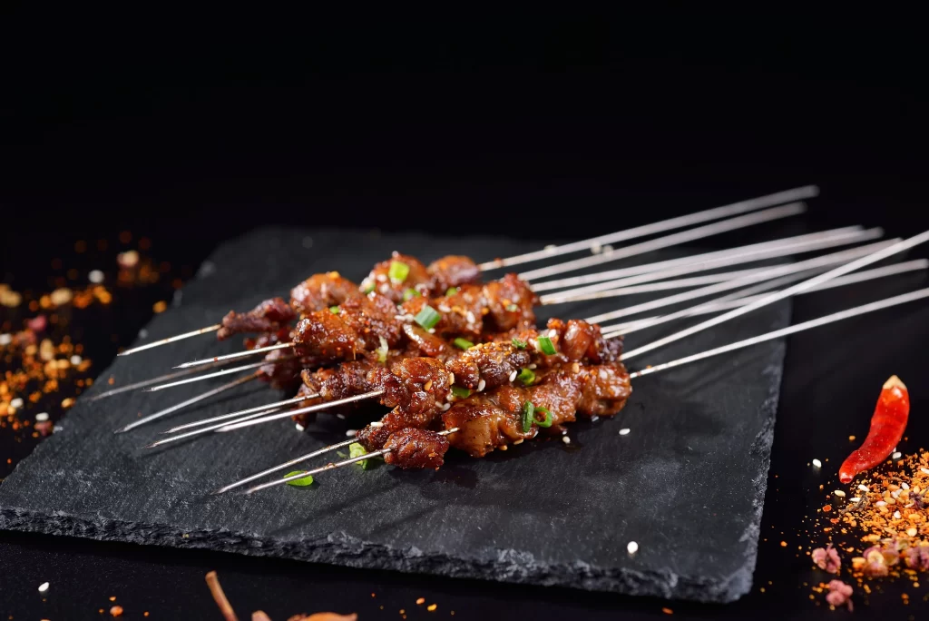 Crispy Pork Skewers Charred Edges Green Onion Garnish Slate Plate
