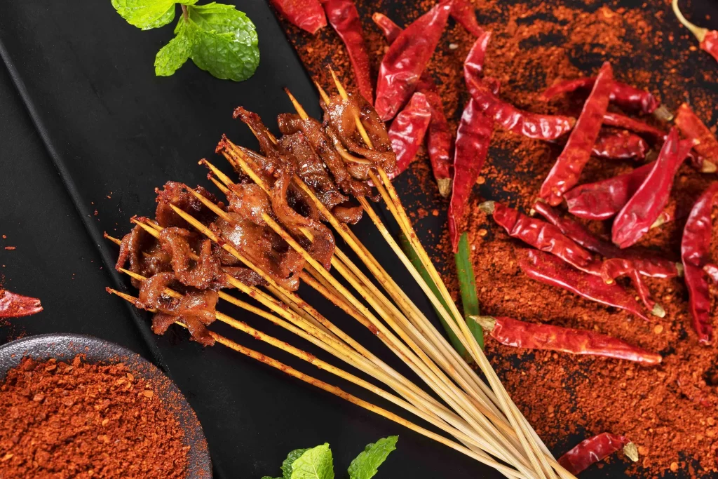 Golden Brown Beef Skewers with Reddish Spices on Black Plate
