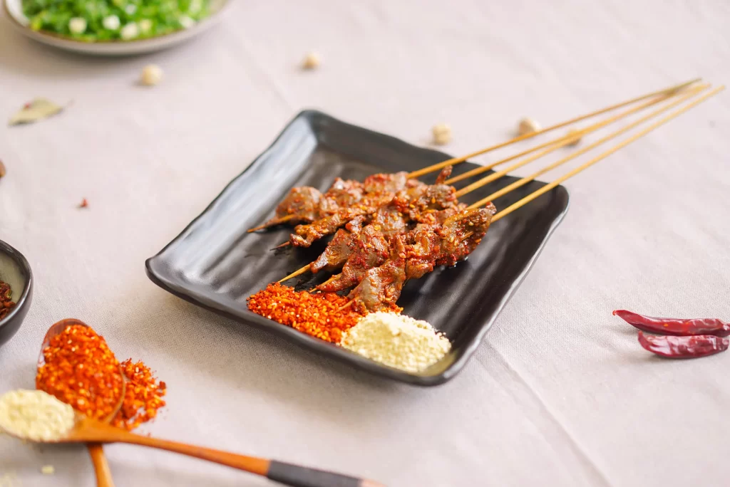 Golden Brown Beef Skewers with Reddish Spices on Black Plate