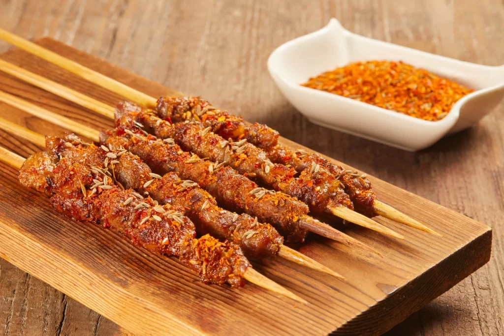 Golden Brown Beef Skewers with Reddish Spices on Wooden Plank
