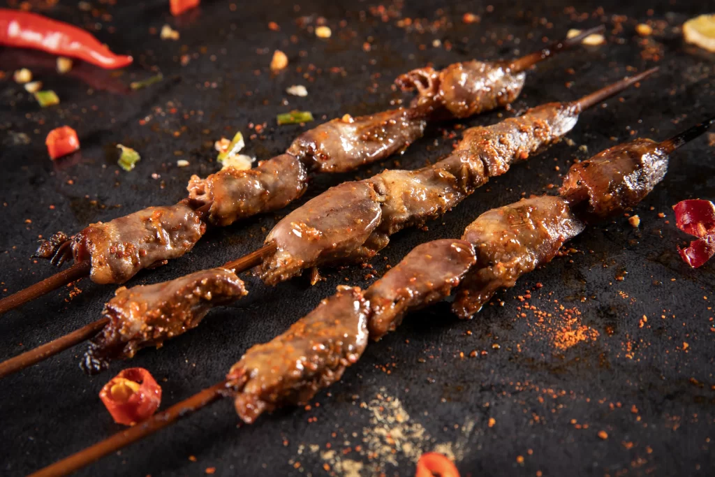 Golden Brown Beef Skewers with Spicy Garnish on Dark Slate