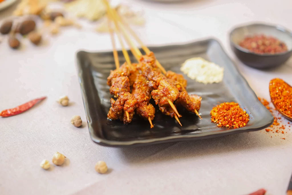 Golden Brown Chicken Skewers on Black Plate with Spices