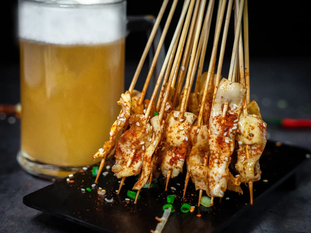 Golden Brown Chicken Skewers with Reddish Spices on Black Plate