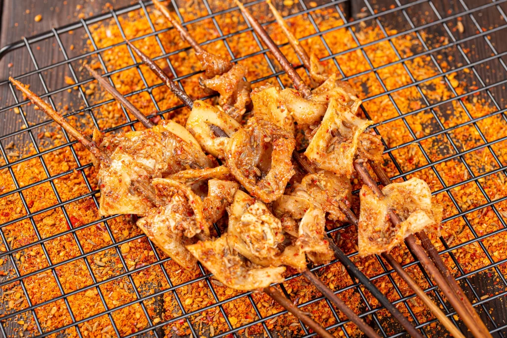 Golden Brown Chicken Skewers with Spicy Red Garnish on Black Grid