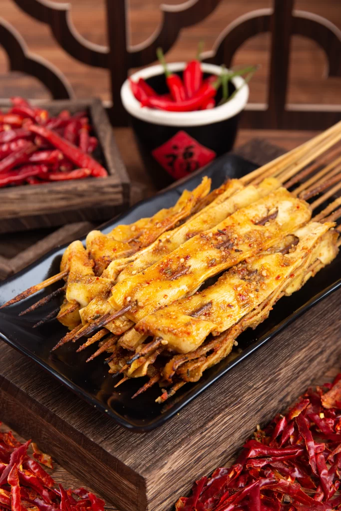 Golden Brown Chicken Skewers with Spicy Red Garnish on Black Plate