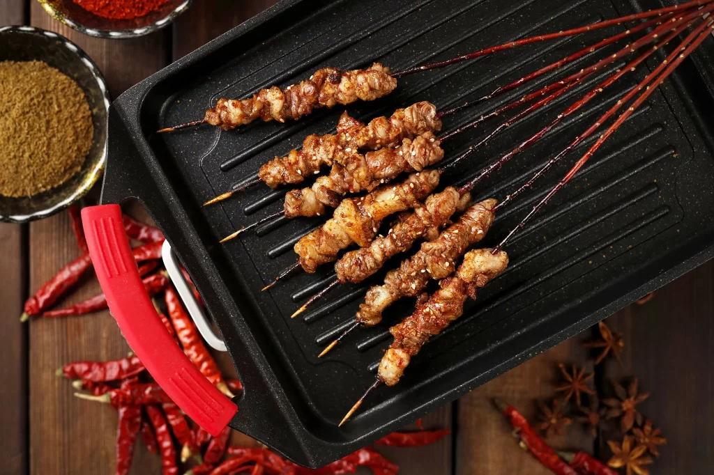 Golden Brown Pork Skewers on Black Grill with Red Handle