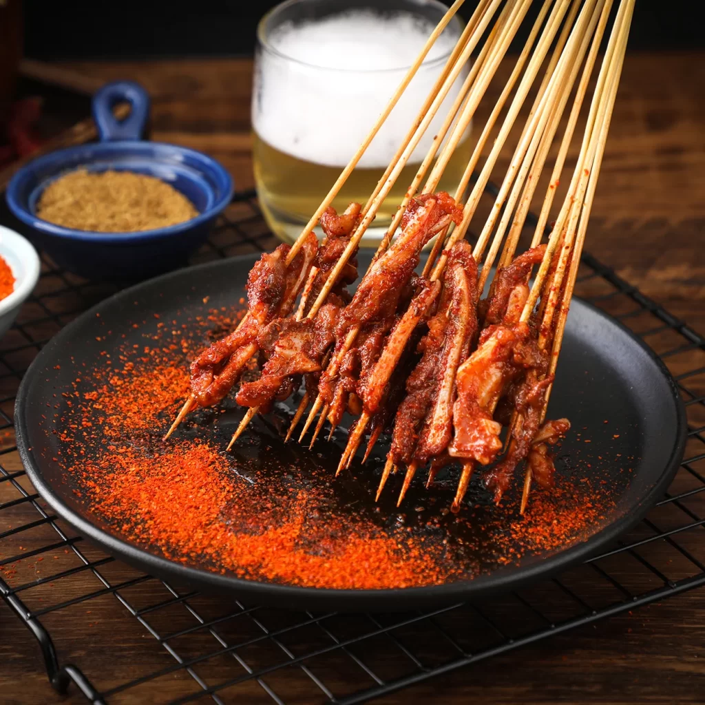 Golden Brown Pork Skewers on Black Plate with Red Pepper Dust
