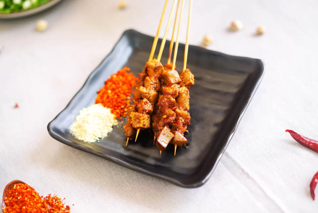 Golden Brown Pork Skewers on Black Plate with Red Pepper Flakes