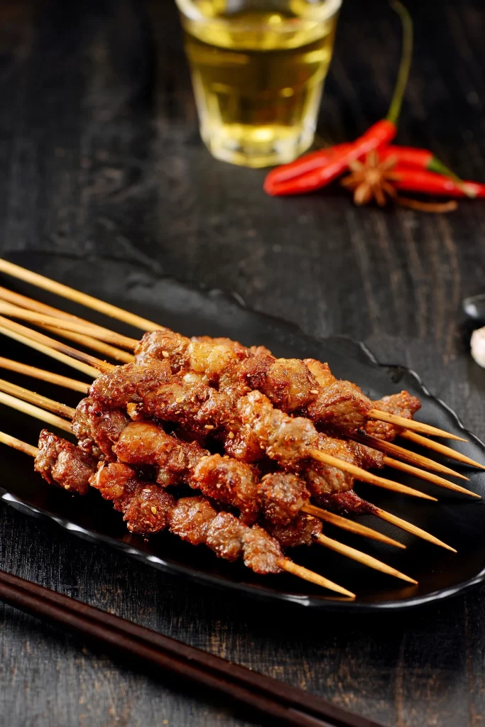Golden Brown Pork Skewers on Black Plate with Reddish Char
