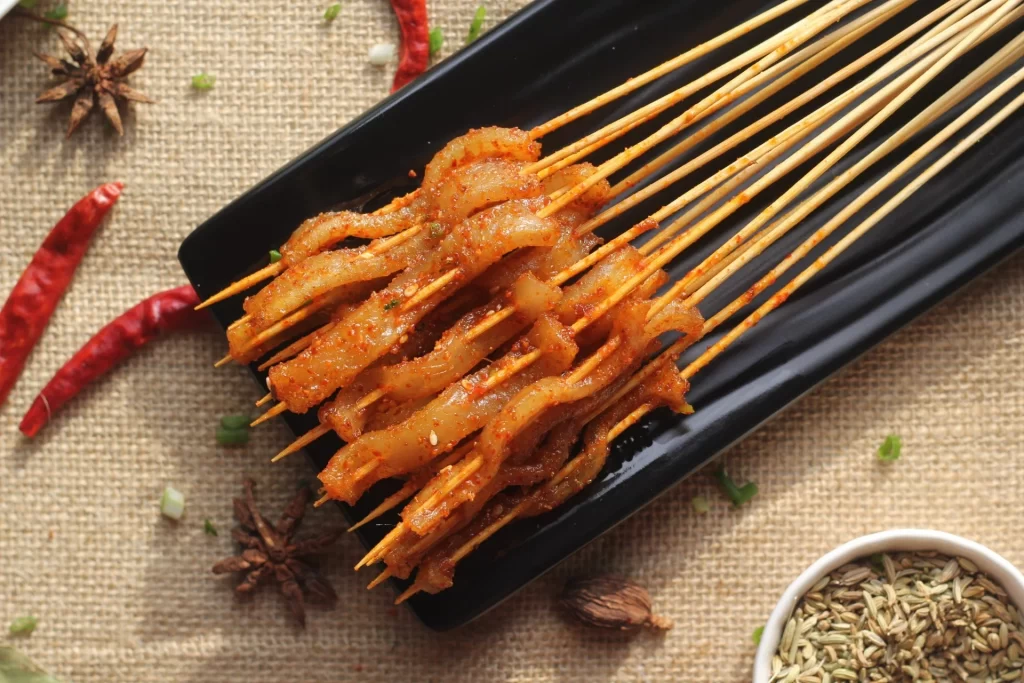 Golden Brown Pork Skewers on Black Plate with Spices