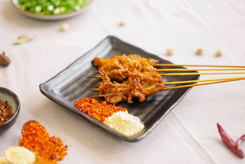 Golden Brown Pork Skewers on Black Plate with Spices
