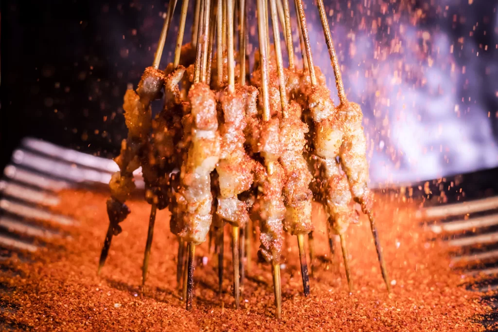 Golden Brown Pork Skewers Sizzling on Black Grill with Reddish Spices