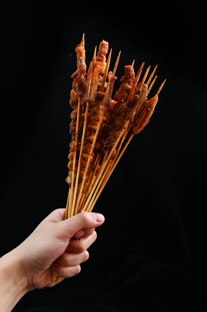 Golden Brown Pork Skewers with Charred Edges on Black Plate