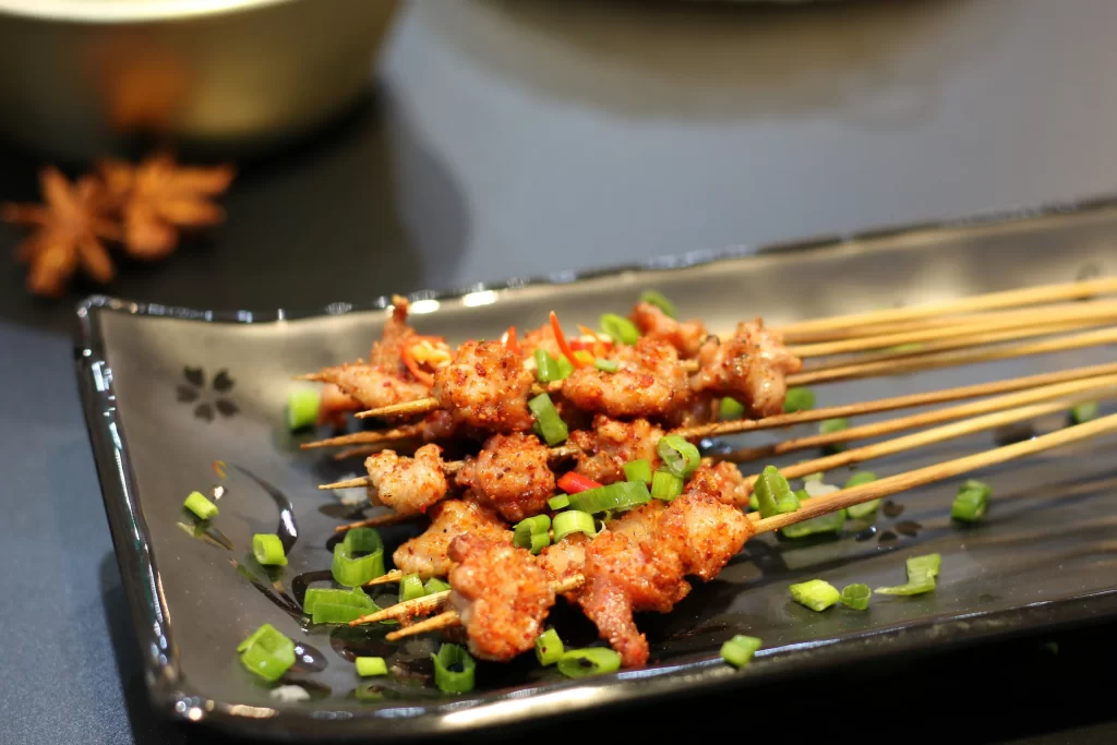 Golden Brown Pork Skewers with Green Onion Garnish on Black Plate