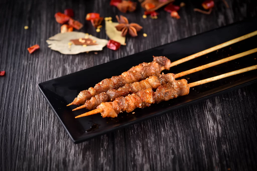 Golden Brown Pork Skewers with Reddish Char on Black Plate