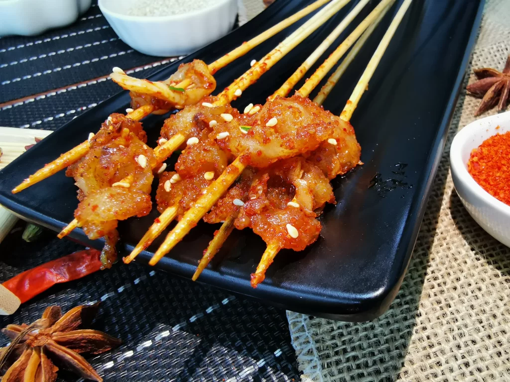 Golden Brown Pork Skewers with Reddish Marinade on Black Plate
