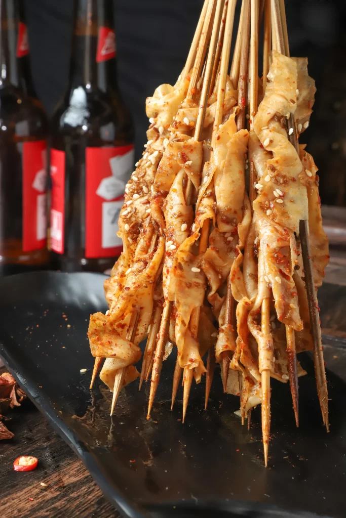 Golden Brown Pork Skewers with Reddish Sauce on Black Plate