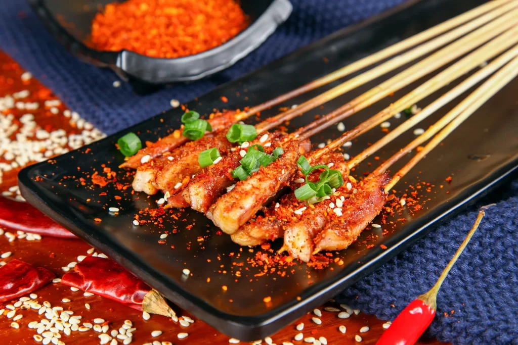 Golden Brown Pork Skewers with Reddish Spice on Black Plate