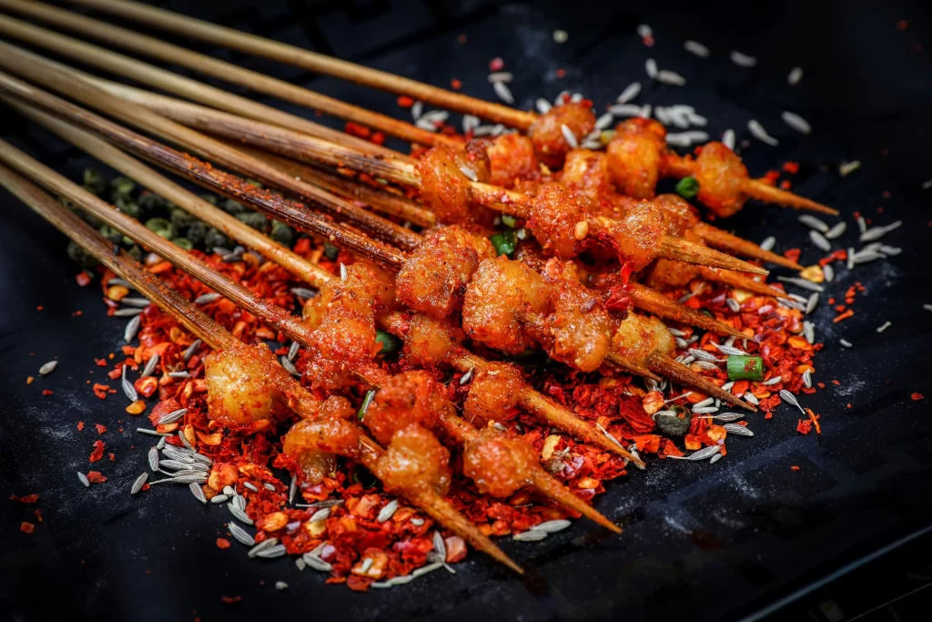 Golden Brown Pork Skewers with Reddish Spices on Black Plate