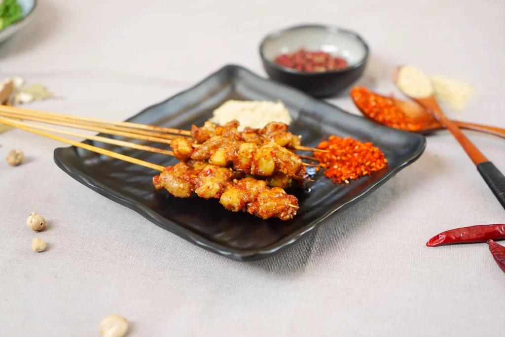 Golden Brown Pork Skewers with Reddish Spices on Black Plate