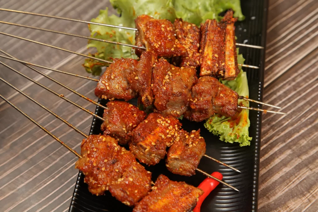 Golden Brown Pork Skewers with Sesame and Lettuce on Black Plate