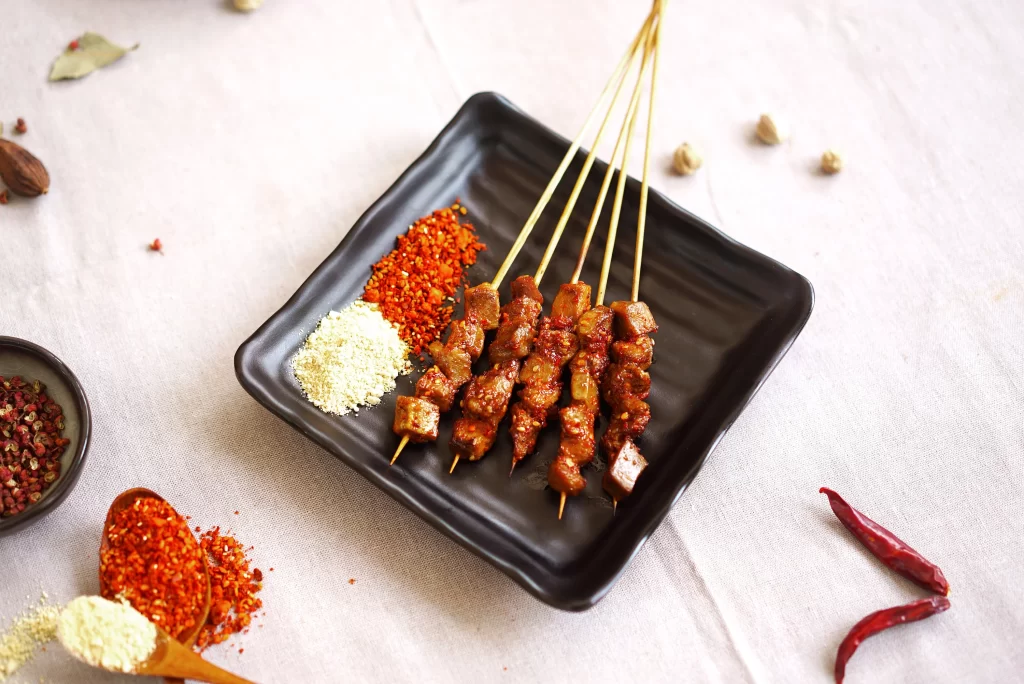 Golden Brown Pork Skewers with Spices on Black Square Plate