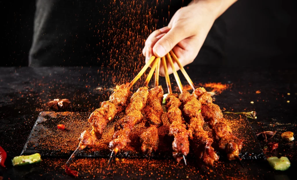Golden Brown Pork Skewers with Spices on Dark Slate Plate