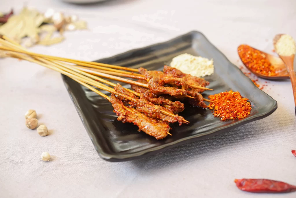 Golden Brown Pork Skewers with Spicy Garnish on Black Plate