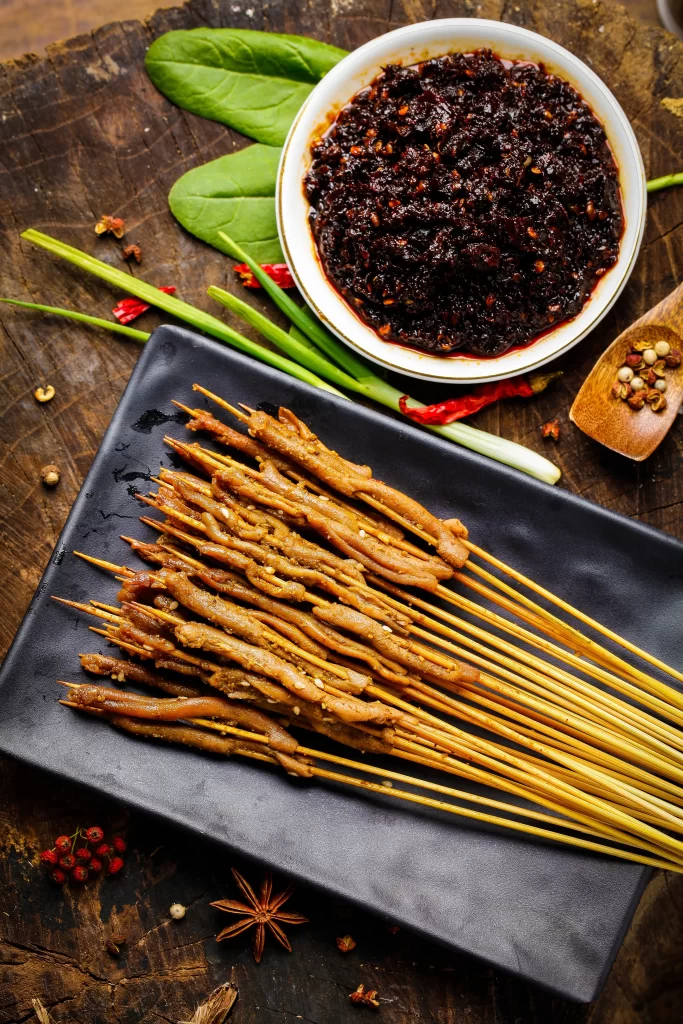 Golden Brown Pork Skewers with Spicy Sauce on Black Plate