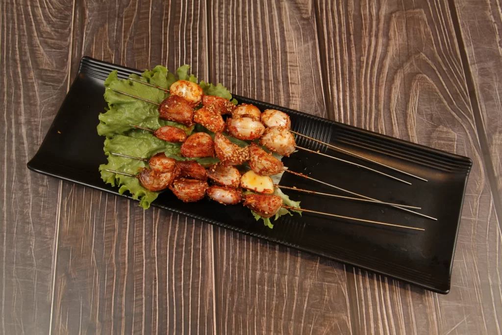 Grilled Pork Skewers with Charred Edges and Green Lettuce Garnish