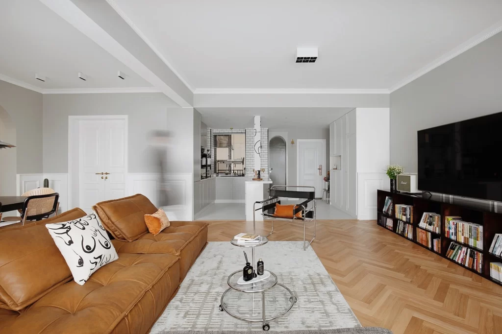 Modern Living Room Neutral Color Palette Brown Leather Sofa Glass Coffee Table White Wainscoting Herringbone Wood Flooring