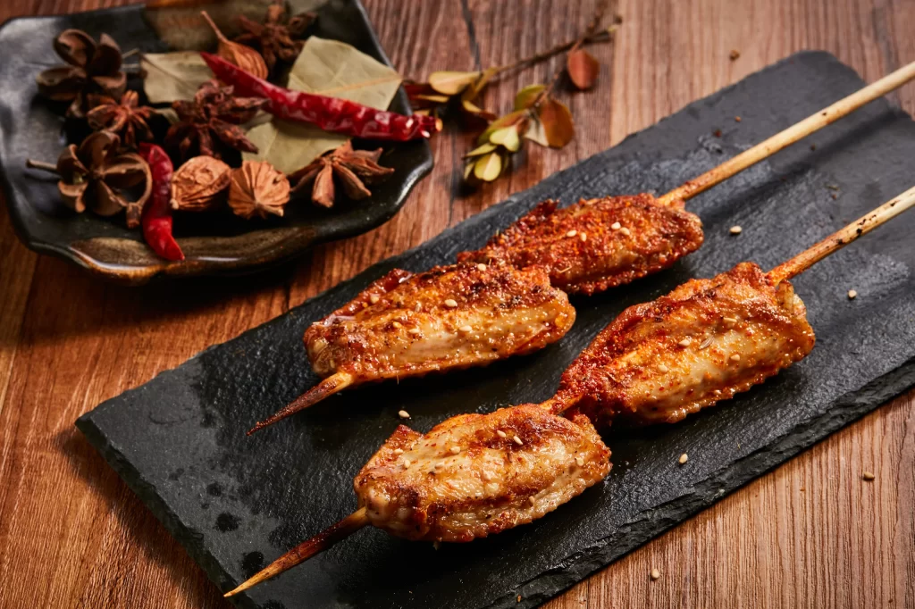 Spicy Chicken Skewers Charred Crust Sesame Garnish Slate Plate